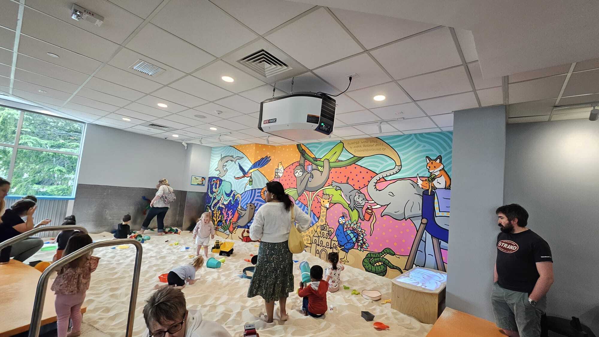 A group of children socializing comfortably whiles playing together in a clean and safe sandmagination's indoor sandbox playground with grafiti painted walls.
