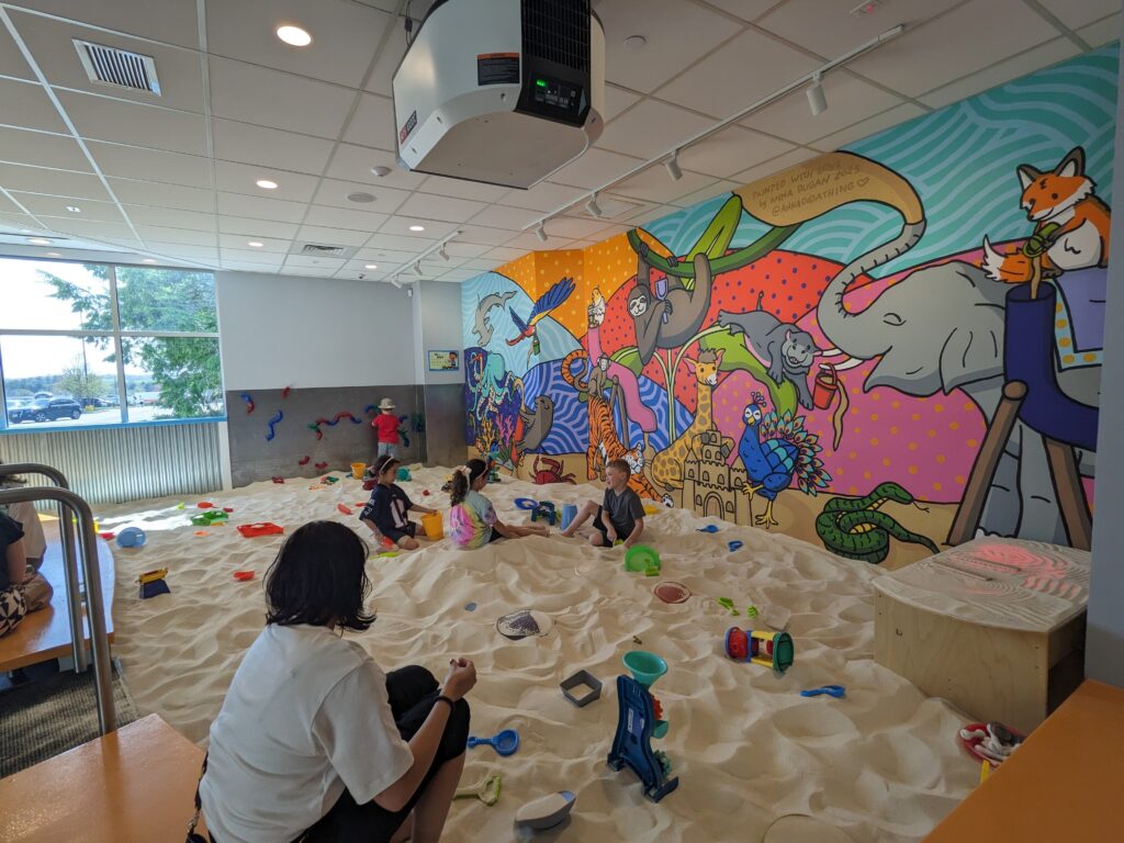 group of children socializing comfortably whiles playing together in a clean and safe sandmagination's indoor sandbox playground with grafiti painted walls.
